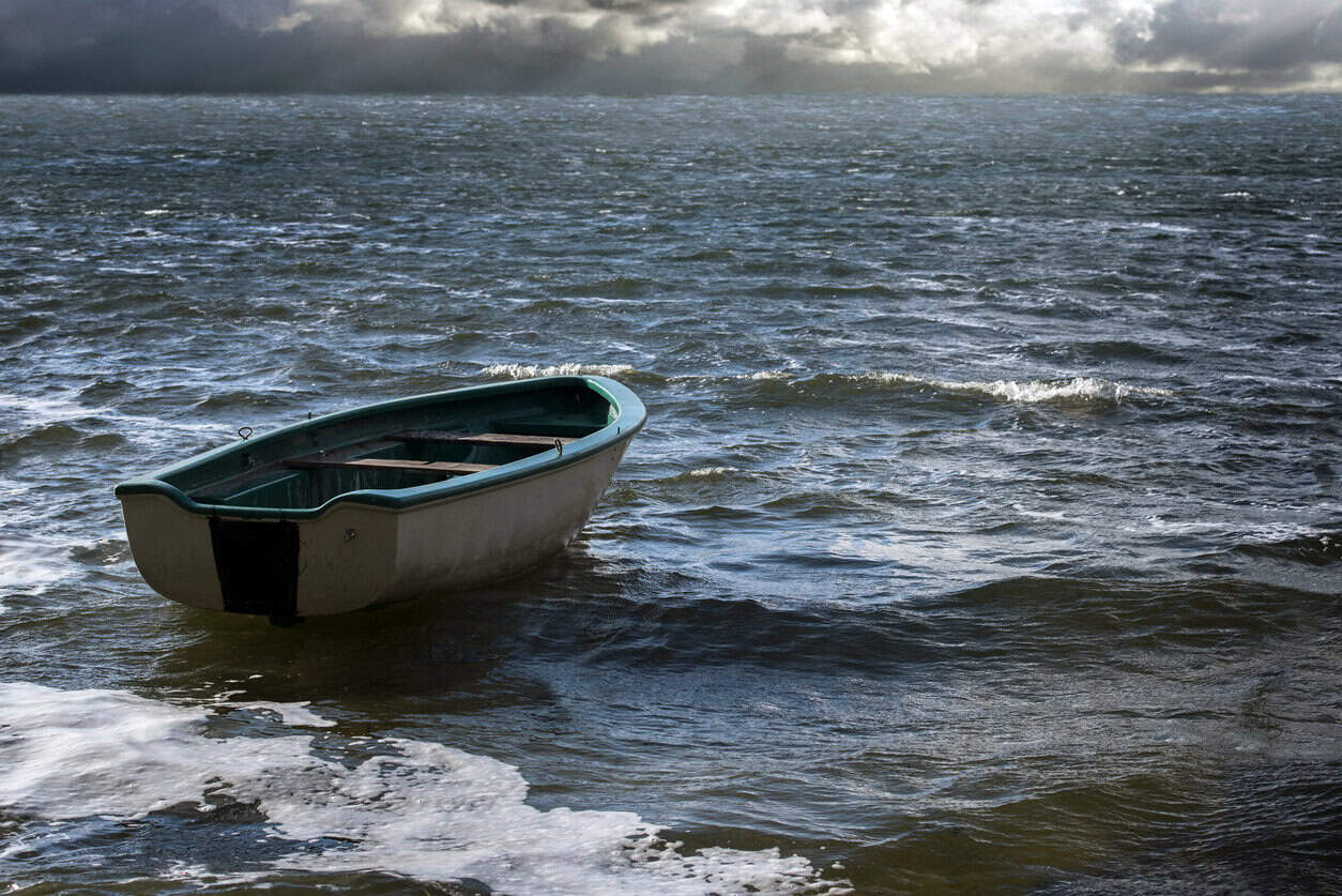 Empty rowboat floats lonely on the sea waves to the clouds at the wide horizon seascape with copy space in the water